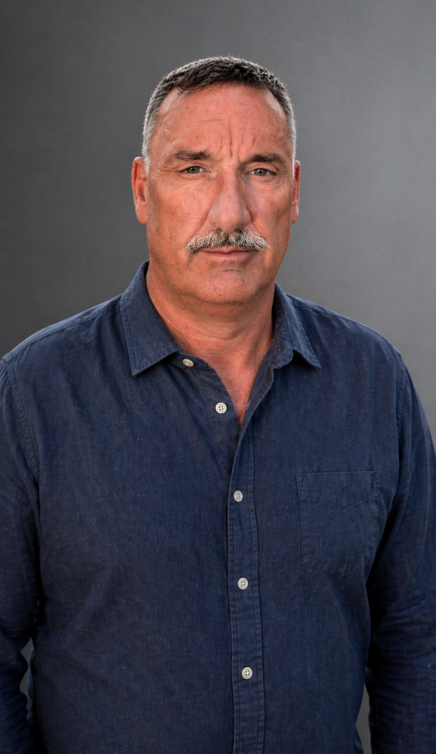 Portrait of a middle-aged man with short gray hair and a mustache, wearing a navy blue button-down shirt, looking at the camera with a neutral expression.