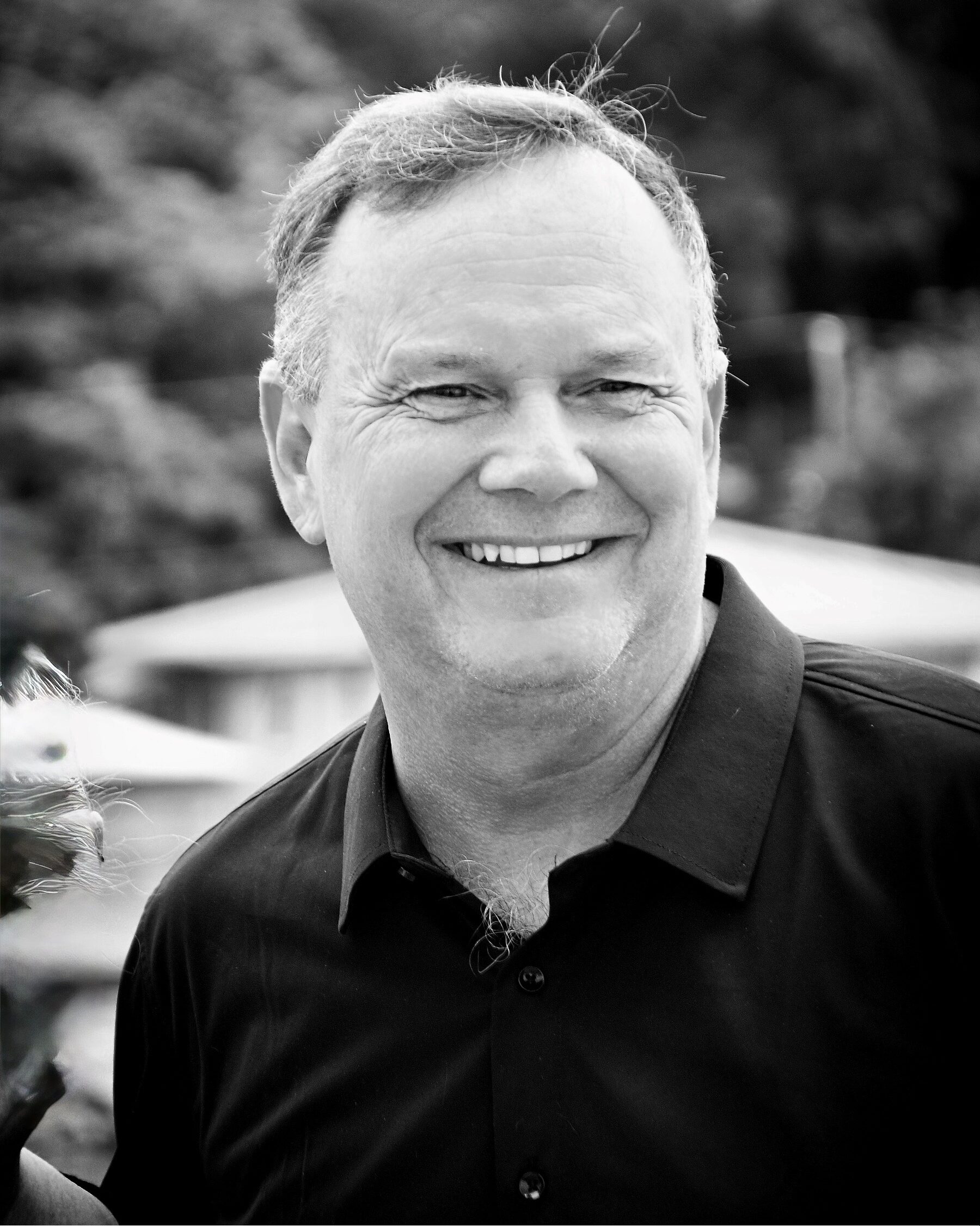 Smiling man in a black button-down shirt photographed outdoors, head and shoulders visible.